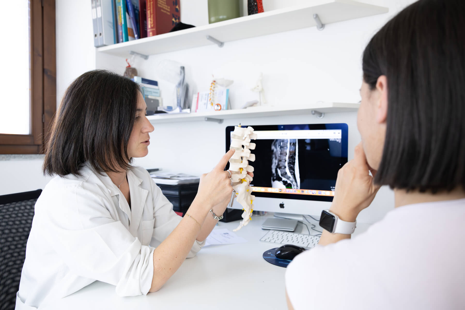 Medico mostra modello anatomico della colonna vertebrale spiegando risonanza al paziente