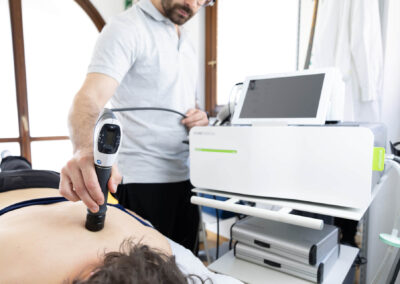 Fisioterapista applica terapia a onde d'urto sulla schiena del paziente durante seduta strumentale