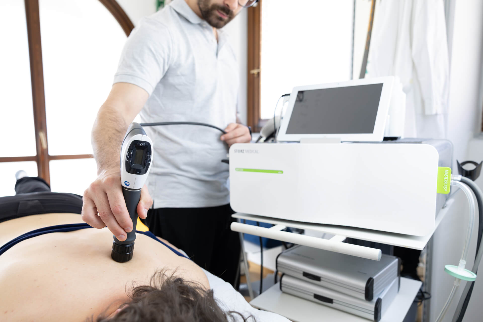 Fisioterapista applica terapia a onde d'urto sulla schiena del paziente durante seduta strumentale