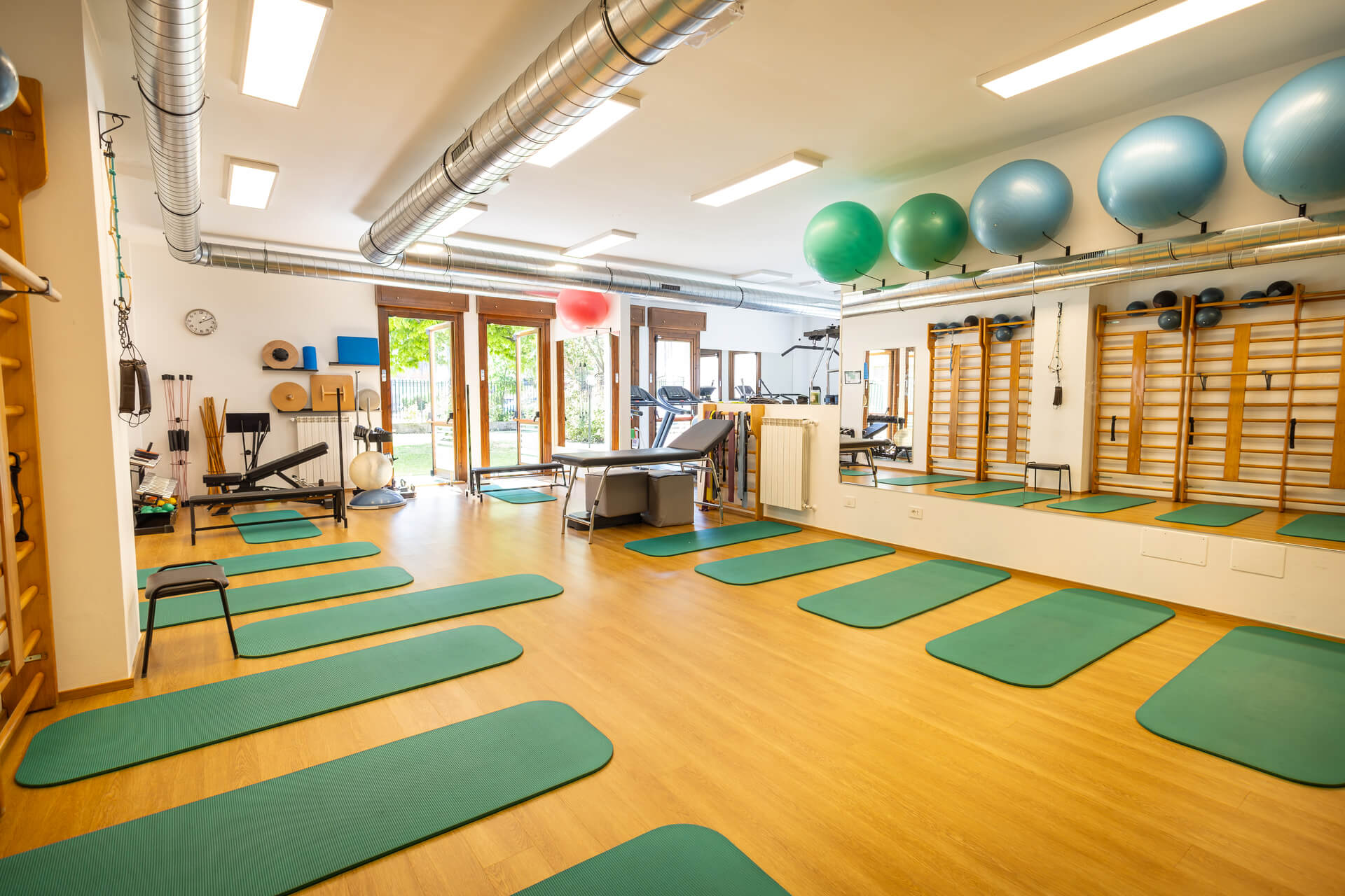 Sala fisioterapia luminosa con fitball, spalliere e tappetini verdi affacciata sul giardino